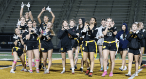 Cheering girls' flag football team celebrating and posing for the camera under stadium lights, showcasing team spirit.