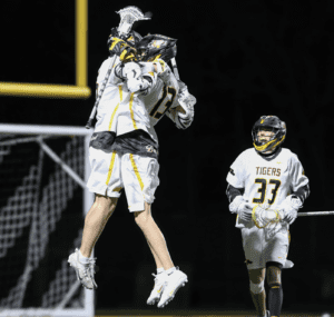 Lacrosse players celebrate a goal with an excited jump during a night game on the field. Team spirit in action!