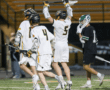 Lacrosse players celebrate a goal during a thrilling game under stadium lights on a turf field.