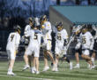 Lacrosse players celebrate a goal during a nighttime game, showcasing teamwork and enthusiasm on the field.