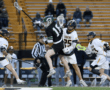 High school lacrosse players compete, showcasing dynamic action on the field during a game. Spectators in the background.