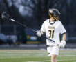 Lacrosse player in white jersey, number 31, holding a stick on the field during a game.
