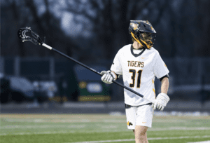 Lacrosse player in white jersey, number 31, holding a stick on the field during a game.