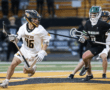 High school lacrosse players in action, with one athlete in white and another in black, competing on the field.