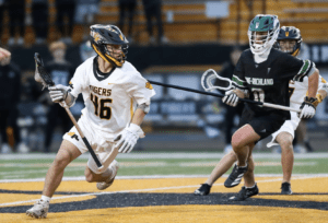 High school lacrosse players in action, with one athlete in white and another in black, competing on the field.