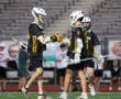 Young lacrosse players in team uniforms shake hands on the field, showcasing teamwork and sport spirit during practice.