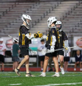 Young lacrosse players in team uniforms shake hands on the field, showcasing teamwork and sport spirit during practice.