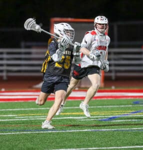 Two lacrosse players compete on a brightly colored field, showcasing athleticism and competitive spirit in a night game.