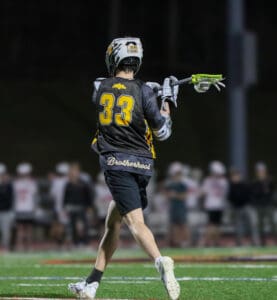 Lacrosse player wearing jersey number 33 passes the ball during a night game, showcasing athletic skill and teamwork.