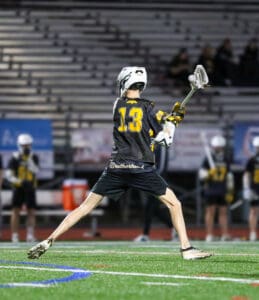 Lacrosse player in action, wearing jersey number 13, preparing to pass the ball on a well-lit field.
