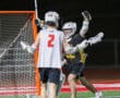 Lacrosse players celebrate a goal at night on a brightly lit field, showcasing teamwork and excitement in the game.