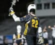 Lacrosse player in jersey number 22 celebrates on the field, holding a stick during an exciting game at night.