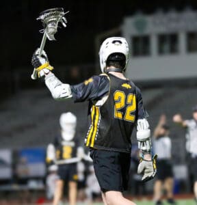 Lacrosse player in jersey number 22 celebrates on the field, holding a stick during an exciting game at night.