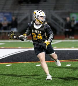 Lacrosse player in black and yellow uniform running on the field, holding a stick with focused determination.