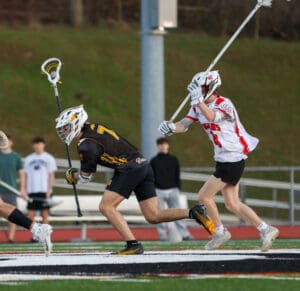 High school lacrosse players compete for the ball on a field, showcasing dynamic action in a competitive game.