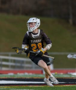 Lacrosse player in action, wearing a Tigers jersey, dribbling a stick on a vibrant field during a game.