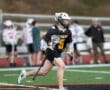 Young lacrosse player in a black Tigers jersey runs on the field, preparing for a play during a game.