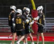 A group of young lacrosse players celebrating a successful play on the field under stadium lights.