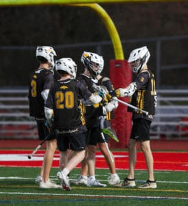 A group of young lacrosse players celebrating a successful play on the field under stadium lights.
