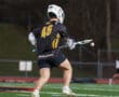 A lacrosse player in action, wearing jersey number 46, prepares to catch a ball during a game on a turf field.