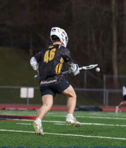 A lacrosse player in action, wearing jersey number 46, prepares to catch a ball during a game on a turf field.