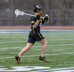 Player in black lacrosse uniform running on field, carrying a lacrosse stick, ready for action in a dynamic game.