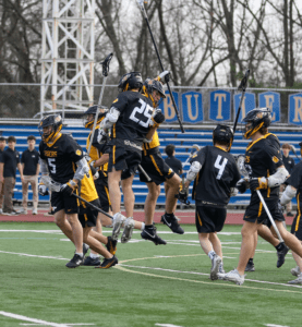 Lacrosse team celebrates a goal on the field, showcasing teamwork and excitement during the match.