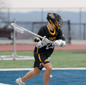 Lacrosse player in black Tigers jersey practicing shots on a field, showcasing athleticism and focus in action.