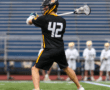 Lacrosse player in action, throwing a ball while wearing jersey number 42 during a game on a turf field.