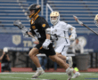High school lacrosse players sprint on the field during a competitive match in athletic gear.