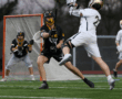 High school lacrosse match in action, with players in black and white jerseys competing for possession on the field.