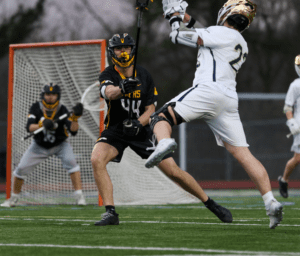 High school lacrosse match in action, with players in black and white jerseys competing for possession on the field.