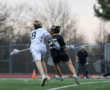 Two young lacrosse players compete for possession on a grassy field during a match, showcasing athleticism and teamwork.