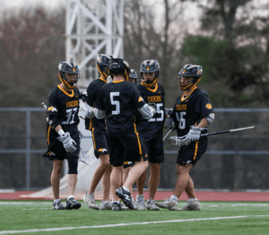 Lacrosse team in black and yellow jerseys celebrates on the field, showcasing teamwork and sportsmanship during a game.