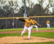 High school baseball pitcher in a yellow Tigers jersey throwing a pitch on the mound, with teammates in the background.