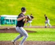 Baseball player in action, preparing to throw the ball at a sunny game with fans in the background.