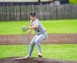 A young baseball pitcher in gray uniform prepares to pitch on the mound during a game on a sunny day.