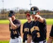 Three baseball players in black jerseys smile and interact on the field, showcasing team spirit and camaraderie.