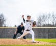 Young baseball pitcher in striped uniform throws a pitch on the mound, with the umpire in the background.