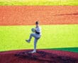 Young pitcher in gray uniform delivers a pitch from the mound on a vibrant baseball field. Sunlight brightens the scene.