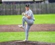 Young baseball pitcher on the mound preparing to throw, wearing gray uniform on a vibrant green field.