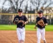 Two young baseball players in black and white uniforms running on the field, preparing for practice.