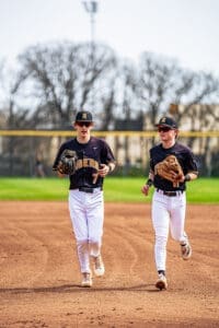 Two young baseball players in black and white uniforms running on the field, preparing for practice.