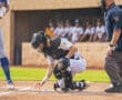 Catcher crouches to retrieve a dropped baseball during an intense moment in a youth baseball game. Umpire observes closely.