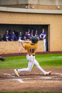 A young baseball player swings at a pitch, showcasing athleticism on the field with teammates in the background.
