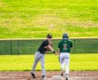 A player in a black jersey throws a baseball to a teammate in green during a sunny baseball game on a grassy field.