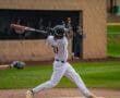 High school baseball player swings a bat, ready to make contact with the ball during a game, with teammates in the background.