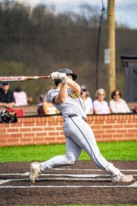 A baseball player swings a bat on the field, aiming to hit a pitch during a game with spectators in the background.