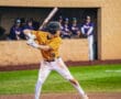 A young baseball player in a yellow jersey prepares to swing a bat, with teammates in the background.