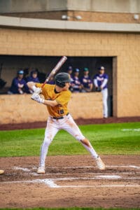 A young baseball player in a yellow jersey prepares to swing a bat, with teammates in the background.